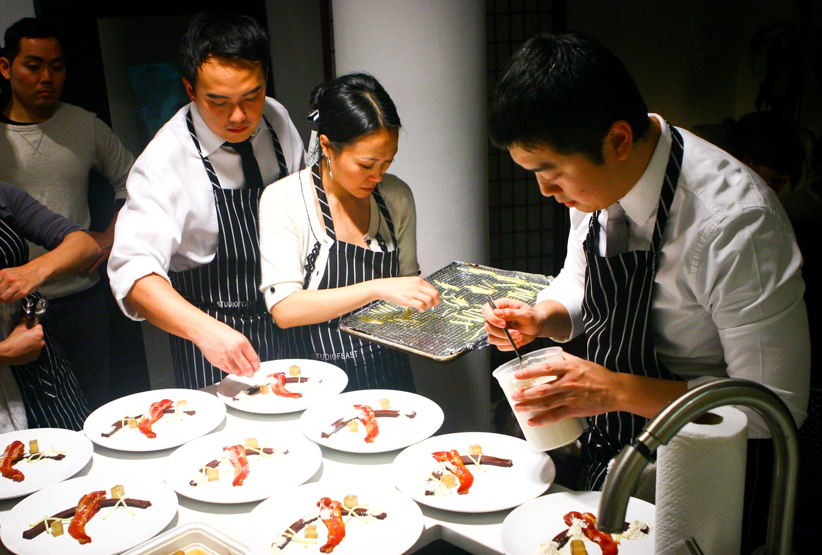 The StudioFeast crew in striped aprons plating a course during a dinner
